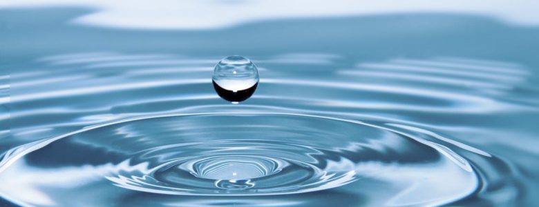 Drop of water falling into bigger puddle of water