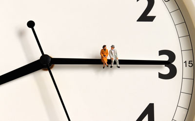 Lomgevity - male and female figures sit on a clock's hour hand