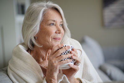 Senior woman cozying up with a cup and throw at home.