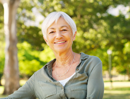 Attractive older woman with gray hair in park with trees