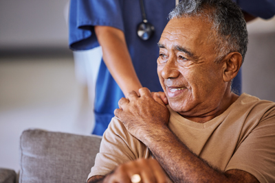 An older man with a caregiver's hand on his shoulder.