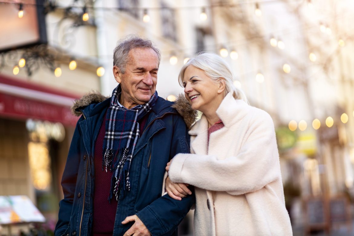 Older couple walking in an urban winter landscape with lights in the background