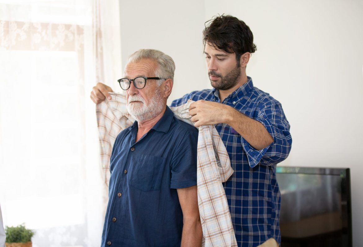 Son putting a shirt around the shoulders of his father living with dementia.