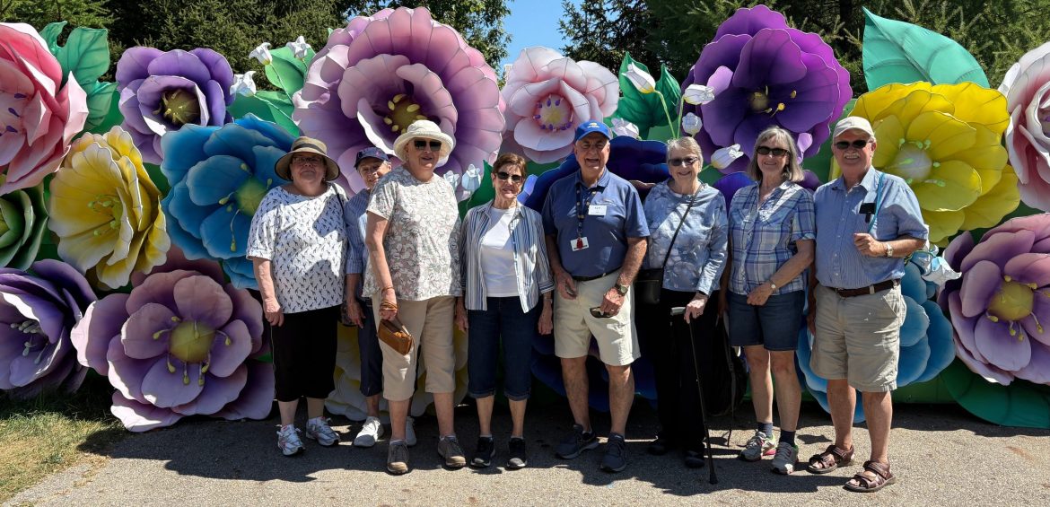 Friendship Village of Dublin Residents pose before a colorful stand of giant flowers during an active adult adventure.