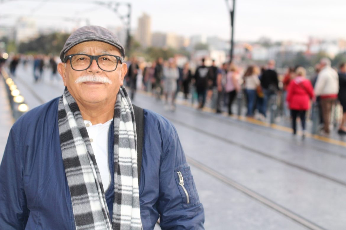 Senior Hispanic man standing near a crowd of people.