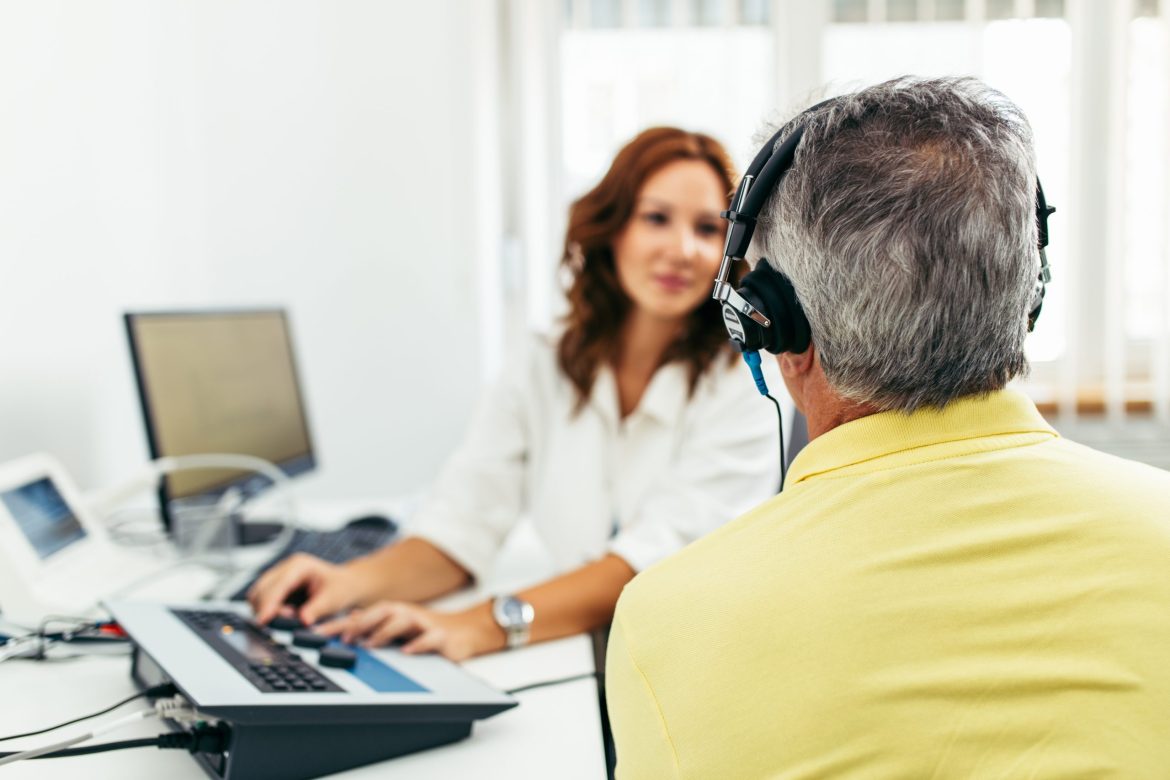 An audiologist administers a hearing test to a gray-haired man.