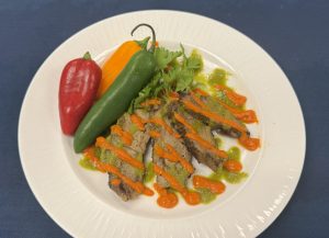 The winning dish at the Taste of New Albany: Montaraz Ibérico Pork Loin with Mojo Verde and Romesco Sauce. Porkchops finely cooked with an orange sauce drizzled over top, with green, orange, and red peppers adorning the side of the dish.