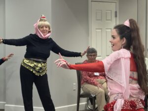 A resident dressed as Jeannie from the classic hit show observes our guest instructor to learn how to bellydance.