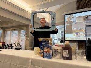 Chef Jim poses behind a TV shaped picture frame following his cooking show display.